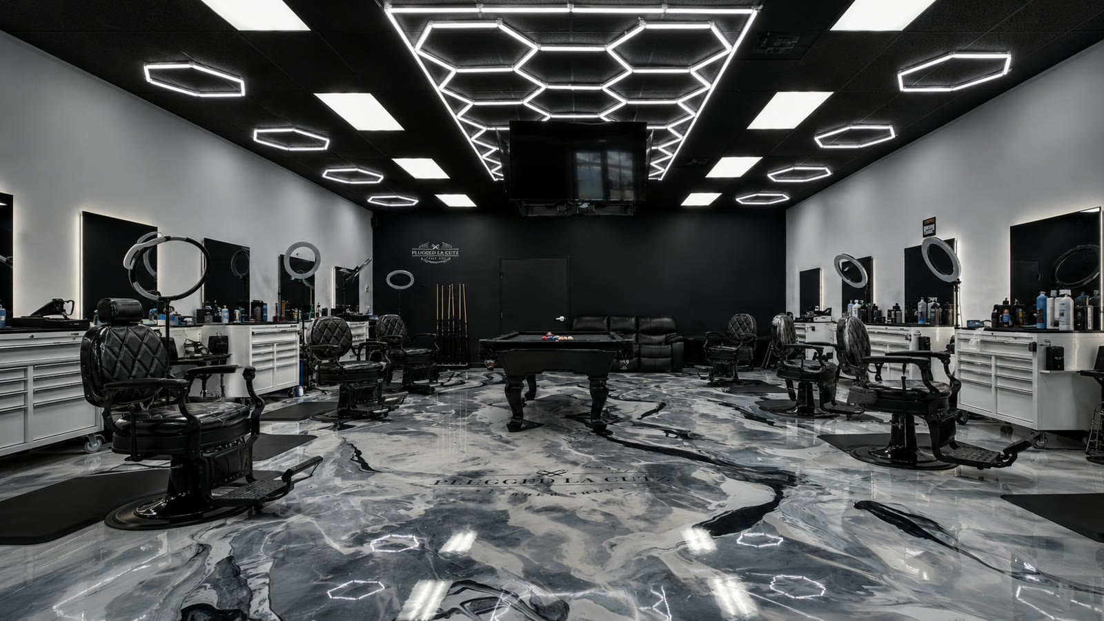 The full Plugged LA Cutz interior: hex-lit ceiling, marble floor, black chairs and pool table.