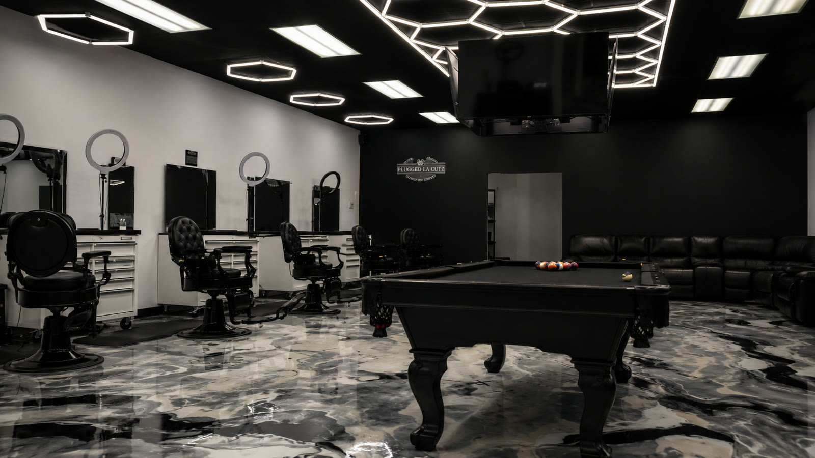 The Plugged LA Cutz floor: black pool table centered on marble, barber stations along the wall, hex lights above.