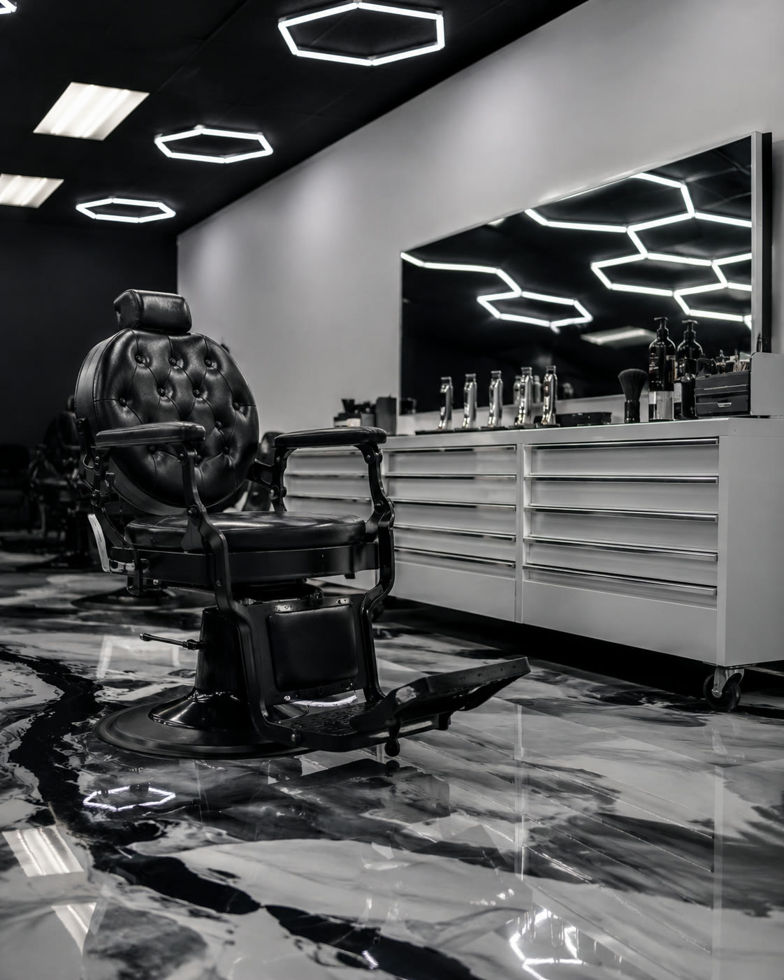 A black tufted barber chair at a white station, clippers lined up beneath the mirror's hex-light reflection.