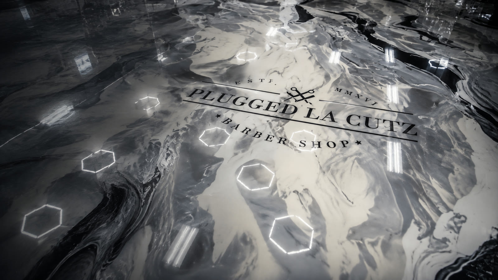 The Plugged LA Cutz name set into the shop's glossy marble floor, reflecting the hexagonal ceiling lights.