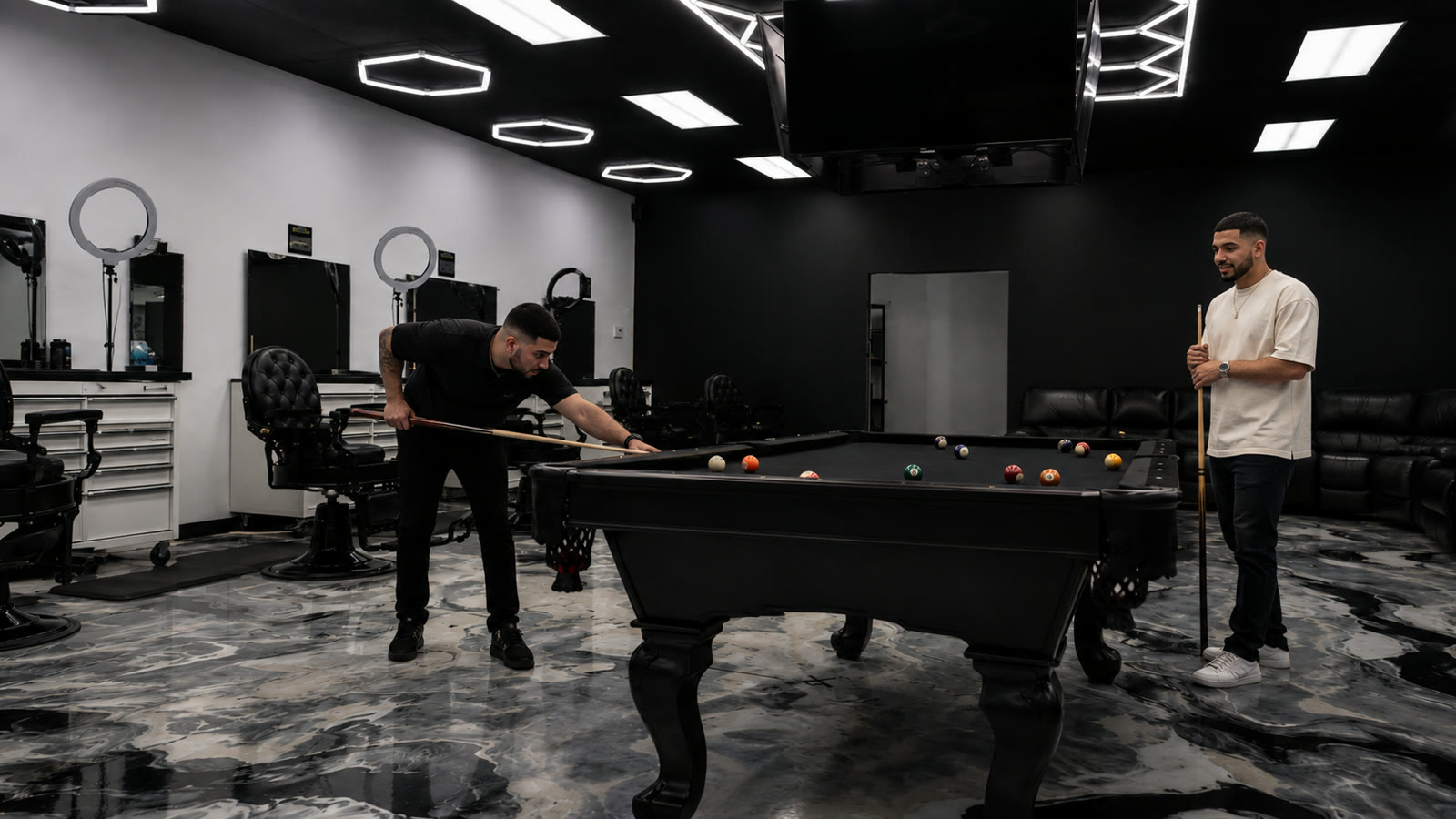 Two clients playing pool on the shop's black table while chairs sit ready along the stations.